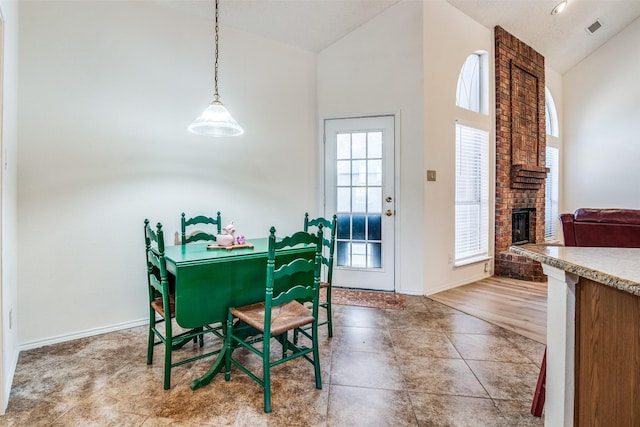 dining area featuring tile patterned floors, high vaulted ceiling, and a brick fireplace