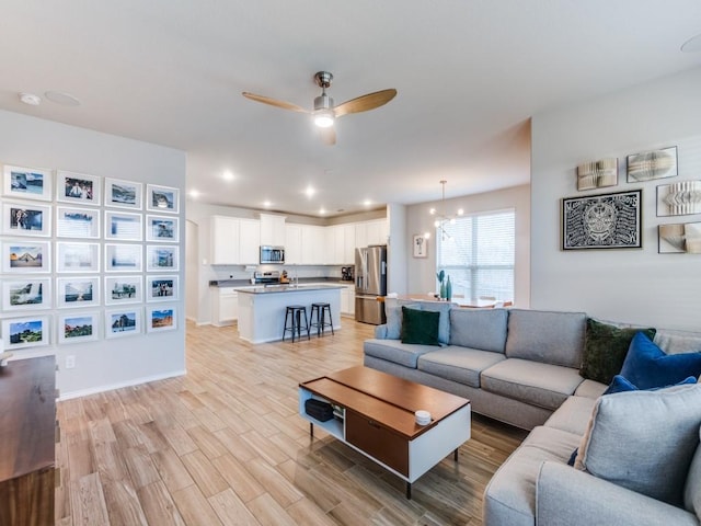 living room with ceiling fan with notable chandelier and light wood-type flooring