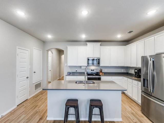 kitchen featuring white cabinets, appliances with stainless steel finishes, light hardwood / wood-style floors, and a kitchen island with sink