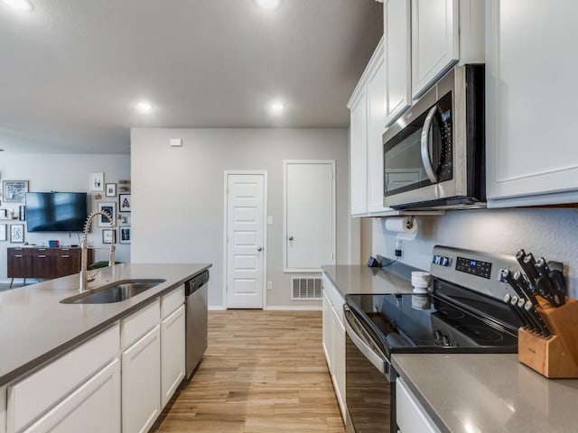 kitchen with stainless steel appliances, white cabinetry, light hardwood / wood-style flooring, and sink