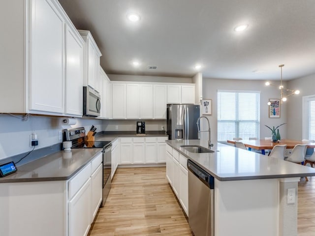 kitchen featuring appliances with stainless steel finishes, an island with sink, pendant lighting, white cabinets, and sink