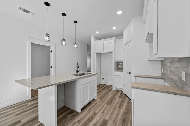 kitchen with sink, tasteful backsplash, white cabinets, and a center island with sink