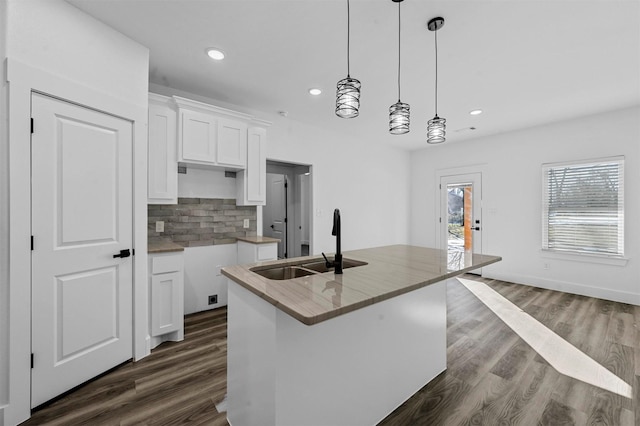 kitchen with hanging light fixtures, a kitchen island with sink, backsplash, white cabinetry, and sink