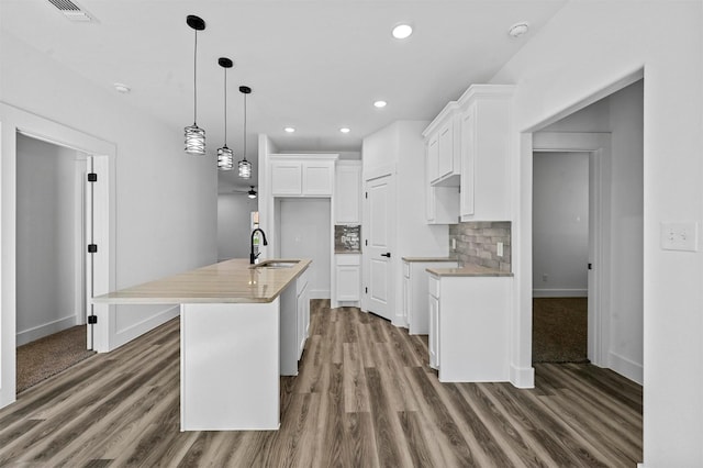 kitchen with a center island with sink, sink, white cabinetry, decorative light fixtures, and tasteful backsplash