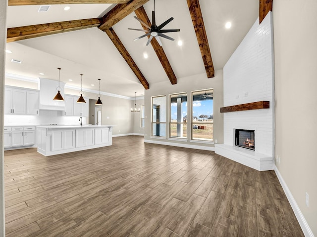 unfurnished living room featuring high vaulted ceiling, beam ceiling, ceiling fan with notable chandelier, a fireplace, and sink