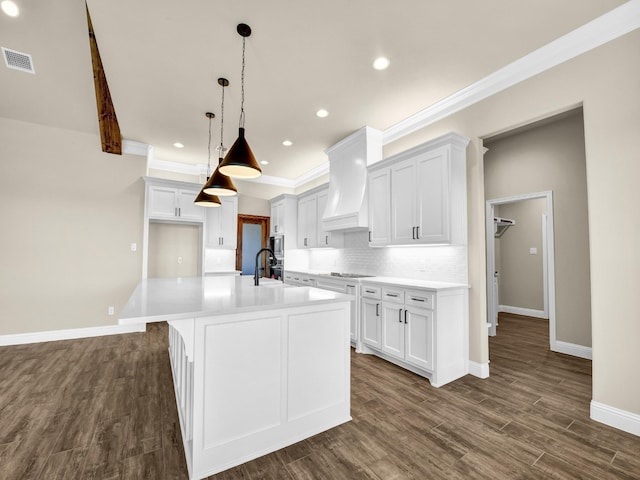 kitchen with white cabinets, pendant lighting, custom exhaust hood, and an island with sink