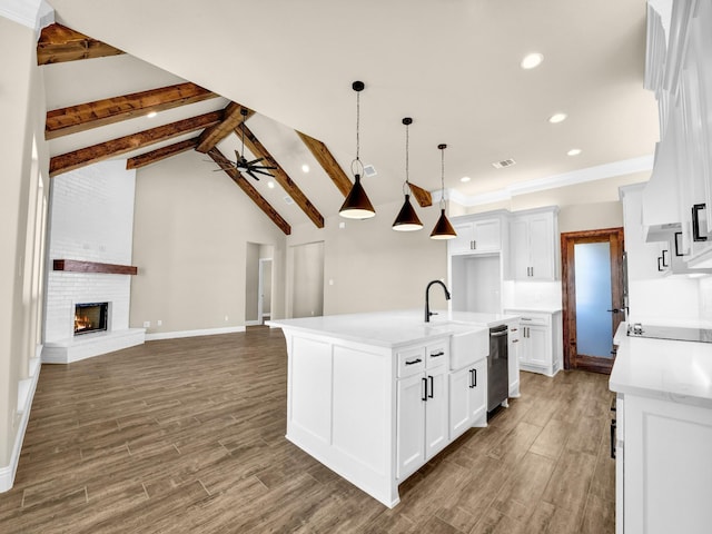 kitchen featuring white cabinetry, ceiling fan, stainless steel dishwasher, a brick fireplace, and a center island with sink