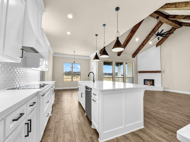 kitchen featuring a large fireplace, a center island with sink, ceiling fan, black electric cooktop, and white cabinets