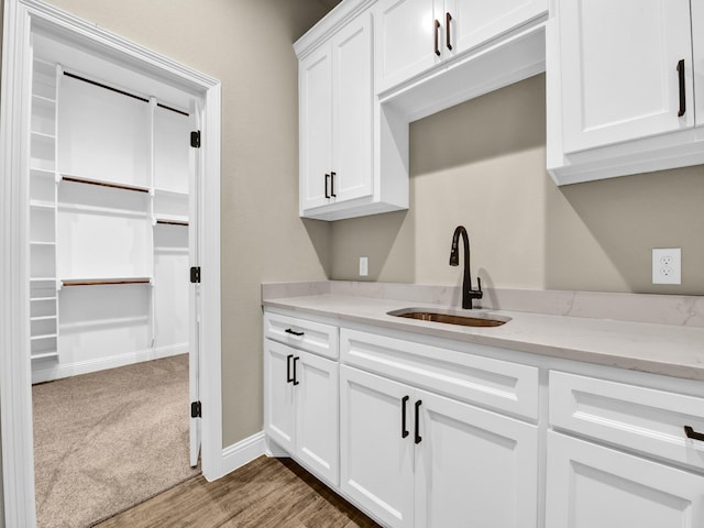 kitchen featuring sink, white cabinets, light stone counters, and carpet flooring