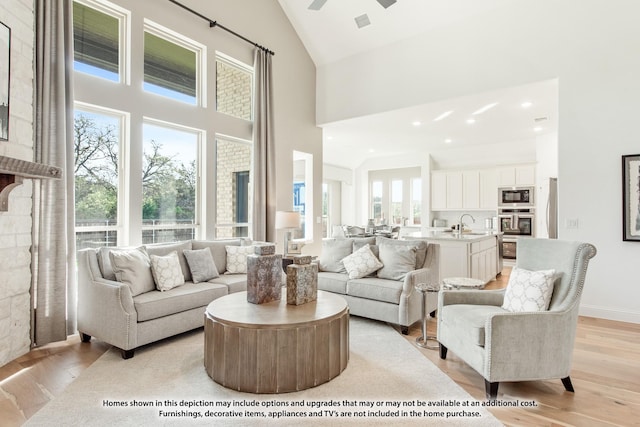 living room featuring light hardwood / wood-style floors, ceiling fan, high vaulted ceiling, and sink