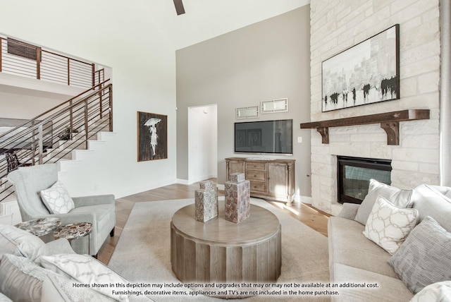 living room with a high ceiling, a stone fireplace, and light hardwood / wood-style flooring