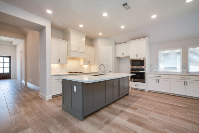 kitchen with oven, white cabinetry, a kitchen island with sink, and built in microwave