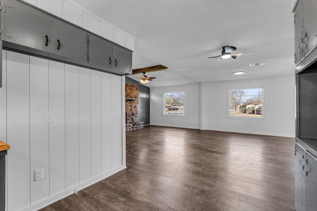 unfurnished living room with a stone fireplace, ceiling fan, beam ceiling, and dark wood-type flooring