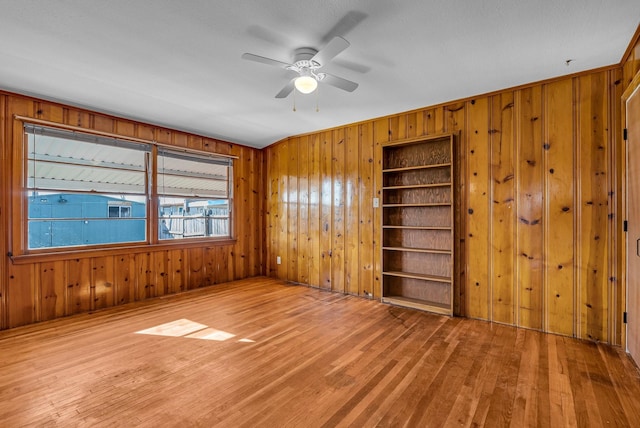 spare room featuring built in shelves, ceiling fan, and light hardwood / wood-style flooring