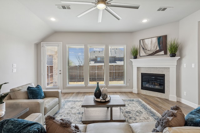 living room with lofted ceiling, a tiled fireplace, ceiling fan, and light hardwood / wood-style floors