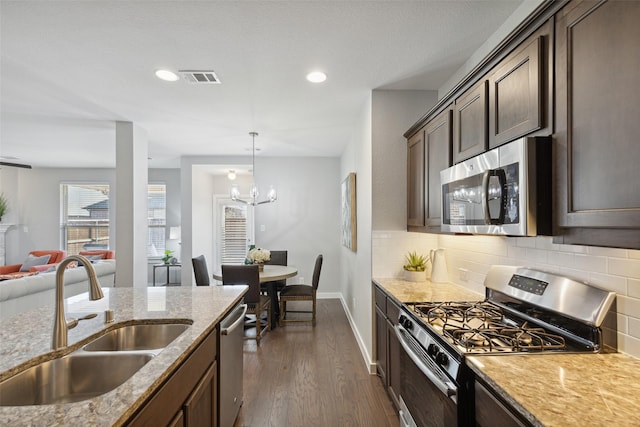 kitchen with stainless steel appliances, sink, an inviting chandelier, light stone counters, and decorative backsplash