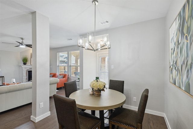 dining space with ceiling fan with notable chandelier, dark hardwood / wood-style flooring, and a fireplace