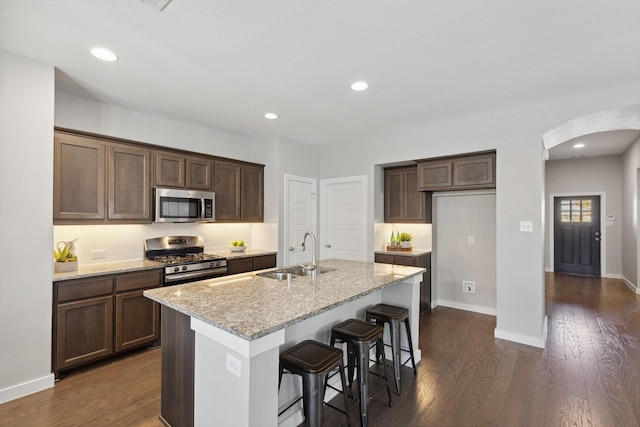 kitchen with a center island with sink, stainless steel appliances, light stone counters, decorative backsplash, and sink