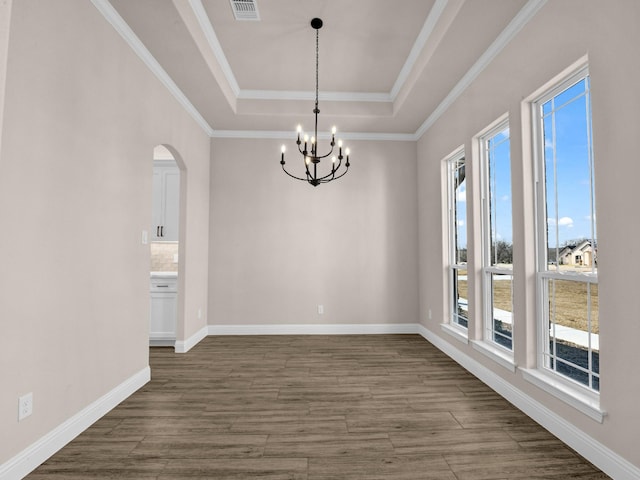 empty room featuring dark wood-type flooring, a raised ceiling, a healthy amount of sunlight, and an inviting chandelier