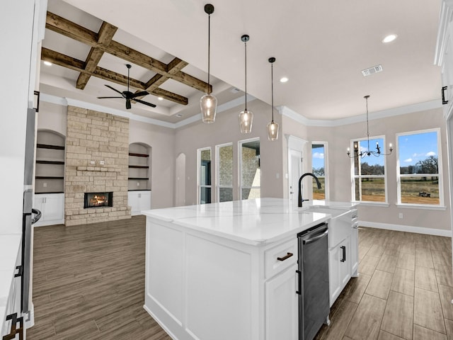 kitchen featuring light stone counters, an island with sink, built in shelves, a fireplace, and coffered ceiling