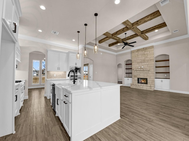 kitchen with stainless steel appliances, white cabinetry, coffered ceiling, a center island with sink, and pendant lighting