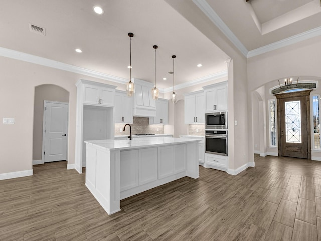 kitchen featuring stainless steel appliances, white cabinetry, tasteful backsplash, and an island with sink