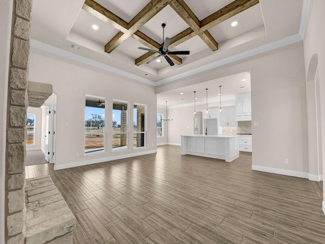 unfurnished living room featuring a towering ceiling, beam ceiling, crown molding, ceiling fan with notable chandelier, and coffered ceiling