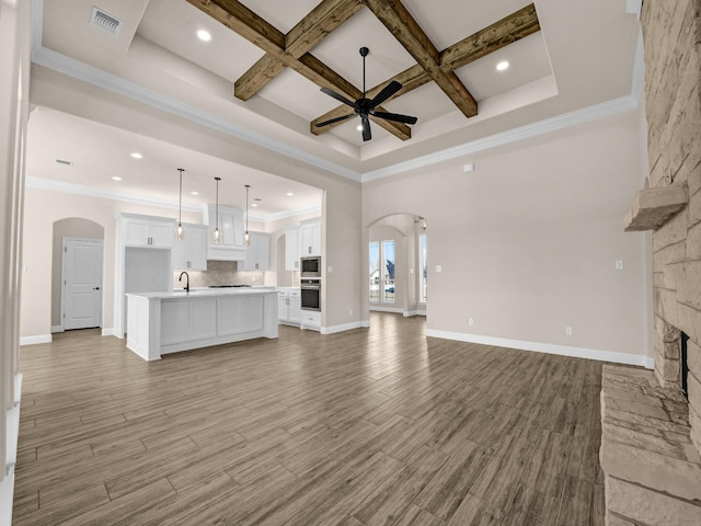 unfurnished living room with coffered ceiling, crown molding, a fireplace, ceiling fan, and beamed ceiling