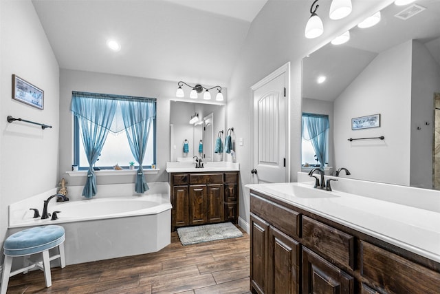 bathroom featuring a tub to relax in, lofted ceiling, and vanity