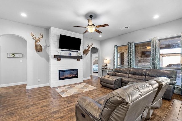 living room featuring a large fireplace, dark wood-type flooring, and ceiling fan