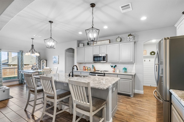 kitchen with sink, decorative light fixtures, backsplash, a center island with sink, and appliances with stainless steel finishes