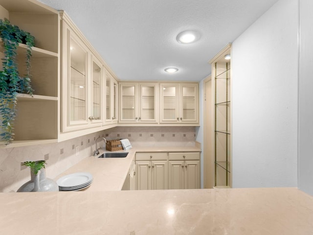 interior space with a textured ceiling, cream cabinets, backsplash, and sink