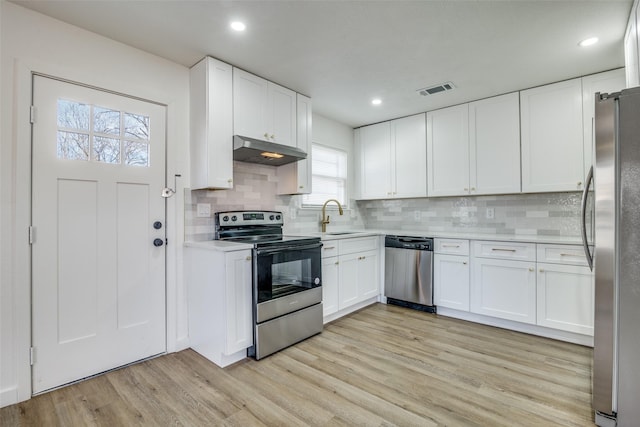 kitchen featuring appliances with stainless steel finishes, sink, white cabinets, light hardwood / wood-style flooring, and tasteful backsplash