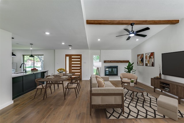 living room featuring lofted ceiling with beams, dark hardwood / wood-style floors, a brick fireplace, ceiling fan, and sink