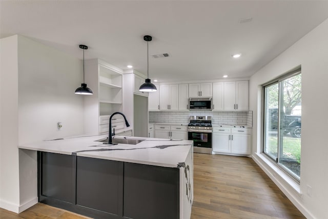 kitchen with appliances with stainless steel finishes, kitchen peninsula, pendant lighting, sink, and white cabinetry