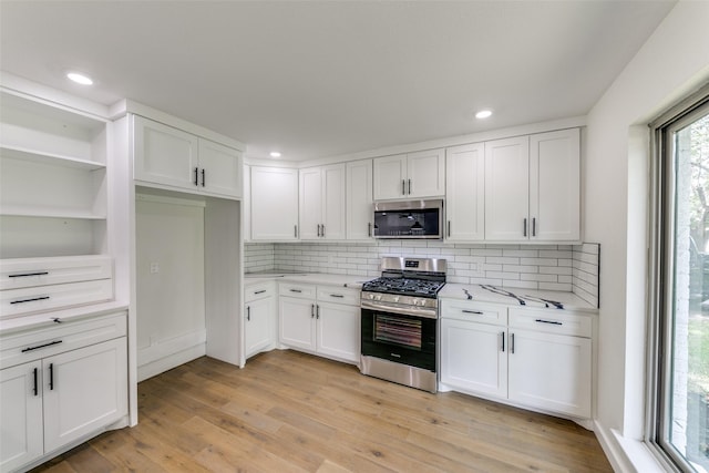 kitchen featuring light stone countertops, light wood-type flooring, backsplash, white cabinets, and appliances with stainless steel finishes