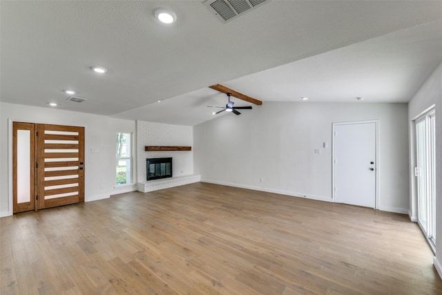 unfurnished living room featuring ceiling fan, light wood-type flooring, a brick fireplace, and vaulted ceiling with beams