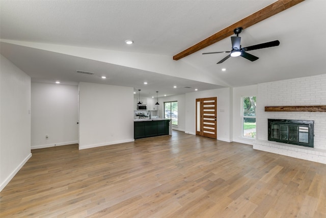 unfurnished living room with ceiling fan, a brick fireplace, light wood-type flooring, and vaulted ceiling with beams