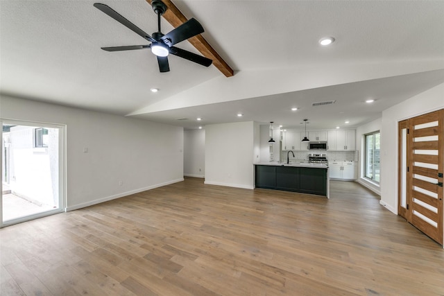 unfurnished living room with ceiling fan, light hardwood / wood-style floors, a healthy amount of sunlight, and vaulted ceiling with beams