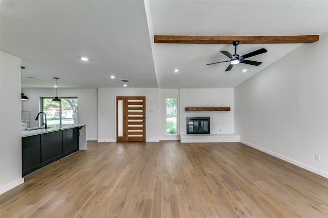 unfurnished living room featuring hardwood / wood-style floors, a fireplace, beam ceiling, and sink