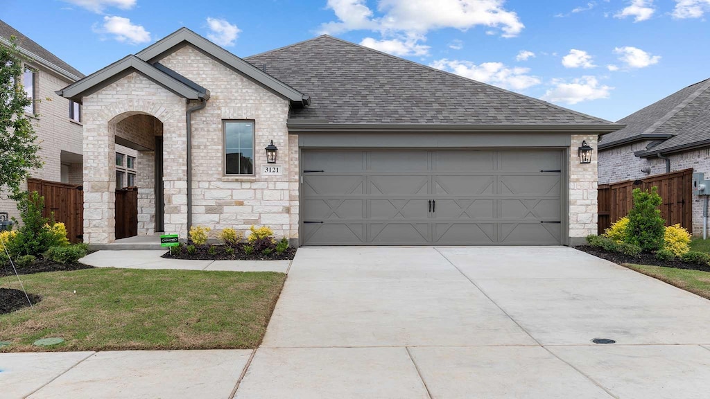 french country style house with stone siding, an attached garage, driveway, and a shingled roof
