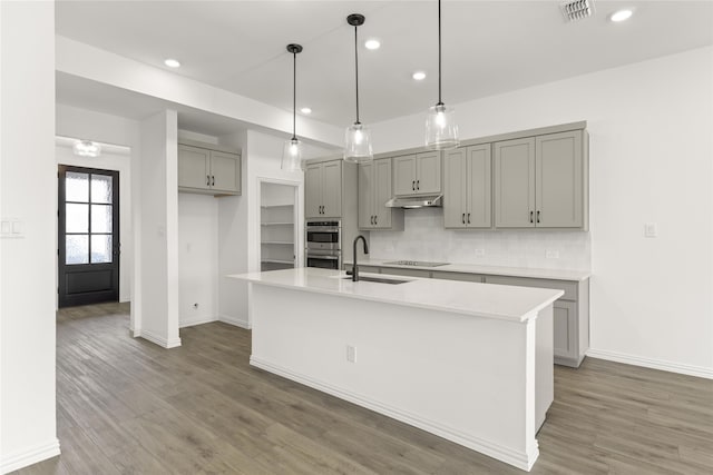 kitchen with gray cabinets, pendant lighting, sink, a kitchen island with sink, and stainless steel double oven