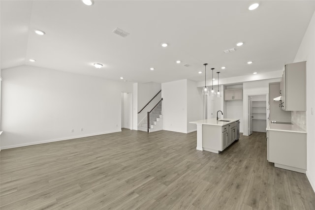 kitchen featuring pendant lighting, sink, hardwood / wood-style flooring, gray cabinetry, and an island with sink