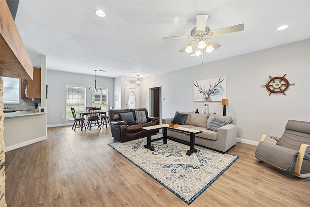 living room with ceiling fan with notable chandelier and light hardwood / wood-style flooring