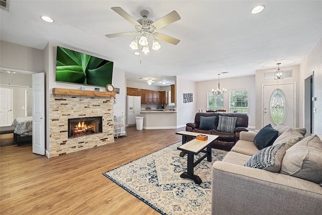 living room with a tiled fireplace, light hardwood / wood-style floors, and ceiling fan with notable chandelier