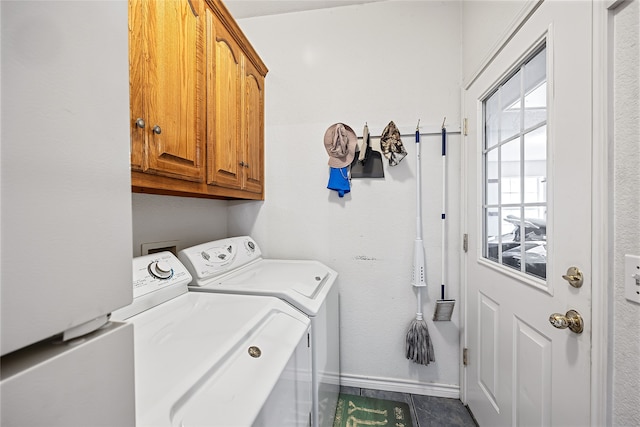 clothes washing area with dark tile patterned floors, washing machine and clothes dryer, and cabinets