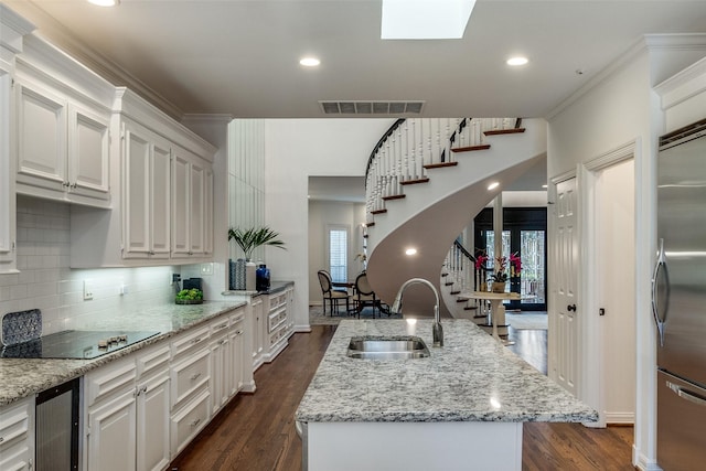 kitchen featuring sink, white cabinets, black electric stovetop, and an island with sink