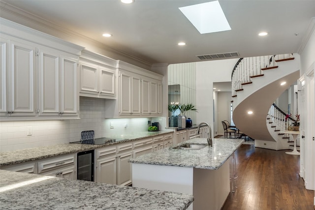 kitchen with sink, white cabinetry, light stone counters, and wine cooler