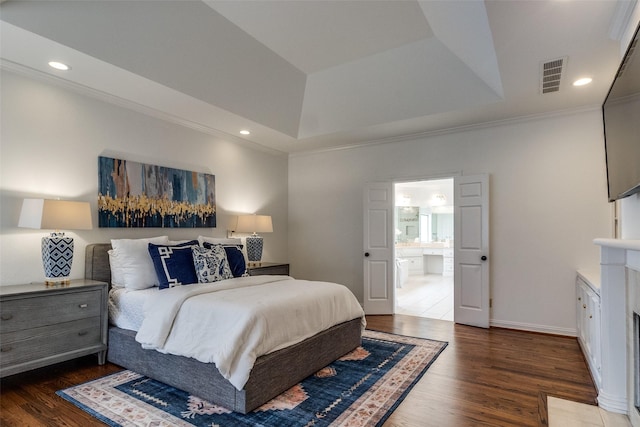 bedroom with ensuite bathroom, dark hardwood / wood-style flooring, ornamental molding, and a tray ceiling