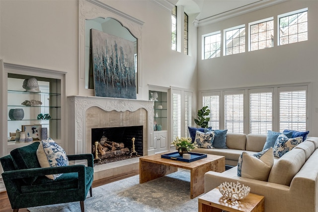 living room with a high ceiling, built in shelves, a high end fireplace, and wood-type flooring